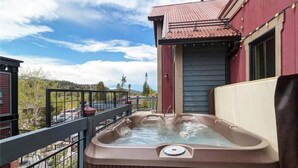 A hot tub on a balcony with a view of a forested area and a building with a red roof. - The Luxurious Lincoln Hot Tub (Breckenridge)