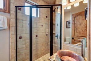 Ein modernes Badezimmer mit einer gläsernen Dusche, einem Kupferspülbecken und einem großen Spiegel.