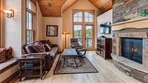 A cozy living room with a fireplace, wooden ceiling, and large windows. - The Luxurious Lincoln Hot Tub (Breckenridge)