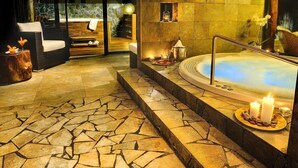 A spa area with a stone-tiled floor, a hot tub, and a seating area with a wooden bench and a wicker chair. - Holiday Home Tatralandia (Liptovsky Mikulas)
