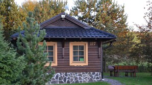 A small wooden cabin with two windows and a stone foundation, surrounded by trees and a bench. - Holiday Home Tatralandia (Liptovsky Mikulas)