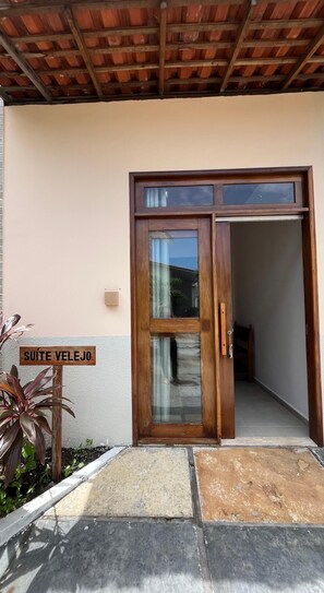 Une porte en bois avec un panneau de verre, une enseigne indiquant « SUITE VELEJO », et une plante placée à côté.