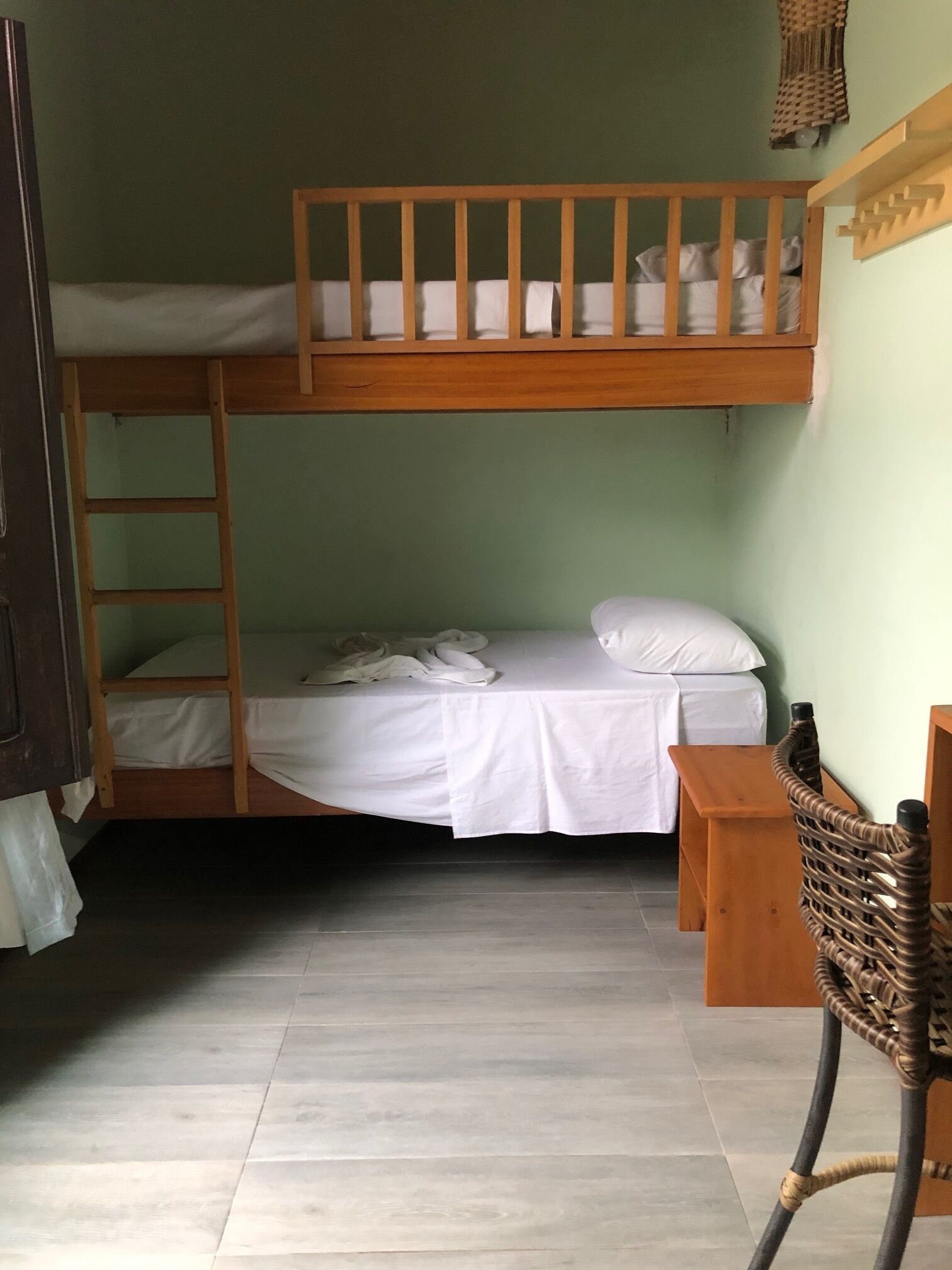 A bunk bed room with a wooden ladder, a small wooden table, and a woven chair.