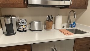 A kitchen with a coffee maker, toaster, knives, paper towel holder, and a sink.