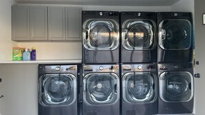 A laundry room with six stacked front-loading washing machines and a shelf with cleaning supplies.