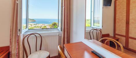 Une pièce comprenant une table à manger, des chaises, une télécommande et une vue sur la mer par une fenêtre.