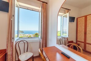 Quarto com uma mesa de jantar, cadeiras, um controle remoto e vista para o mar através de uma janela.