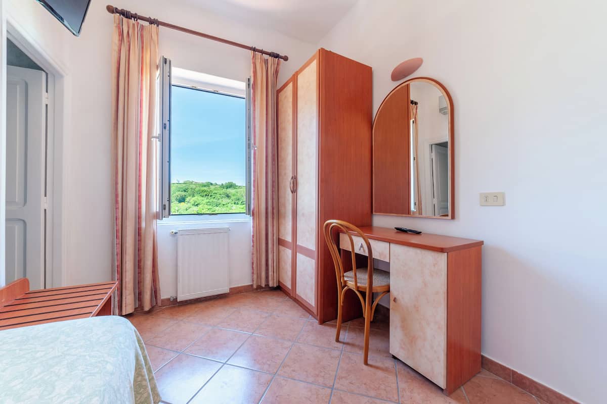 Een slaapkamer met een bed, een bureau, een stoel, een spiegel en een raam met gordijnen.