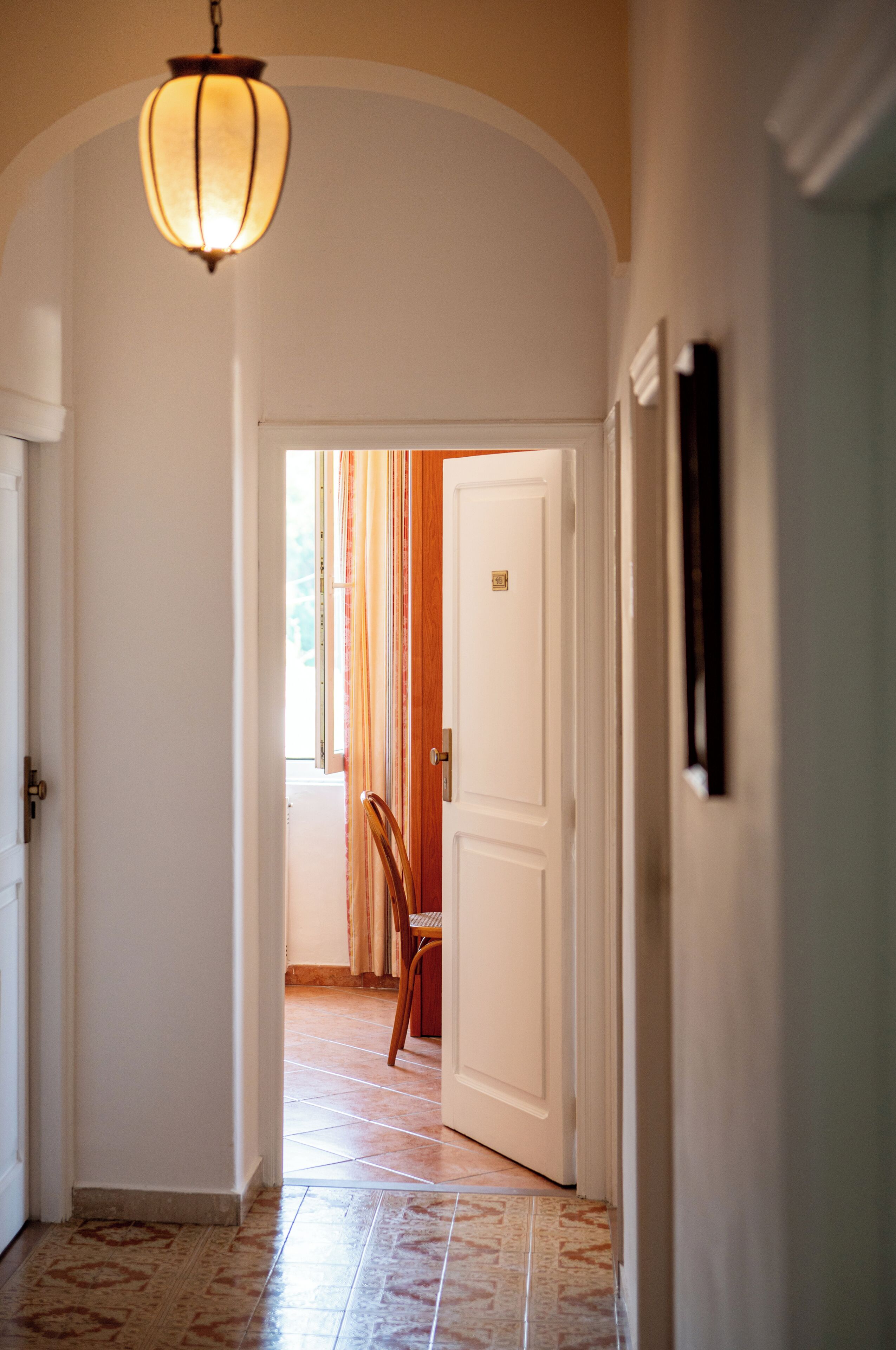 A hallway with a white door, a hanging light fixture, and a chair.