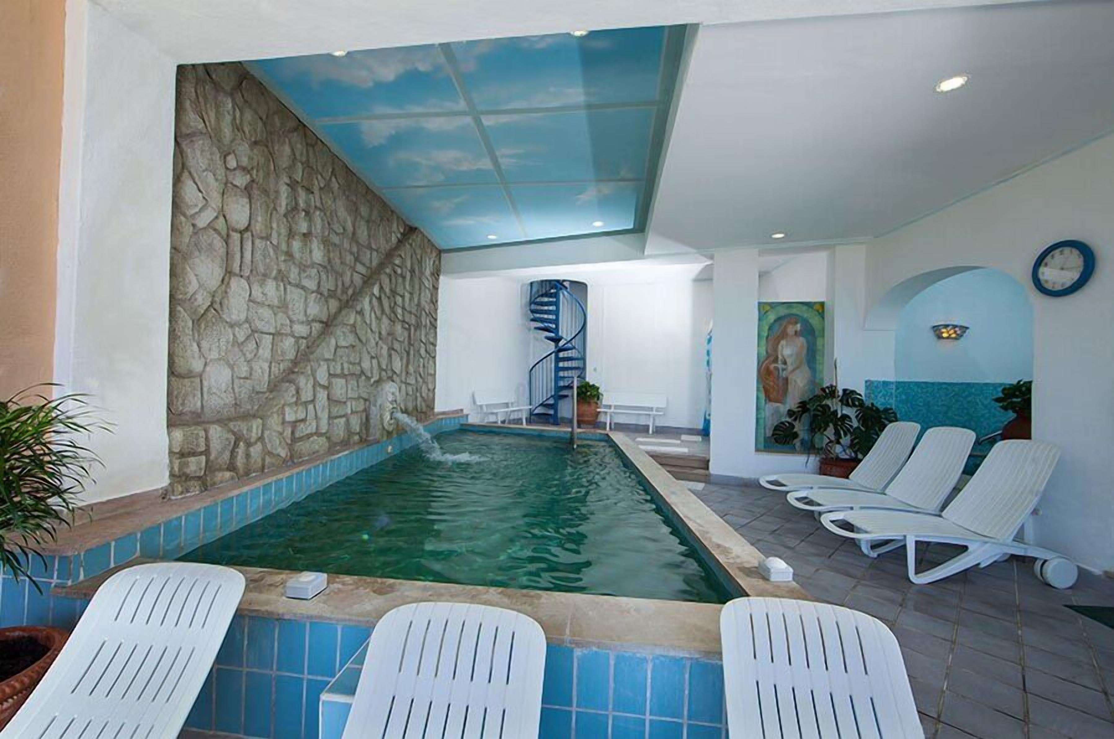 An indoor swimming pool with a stone wall, a spiral staircase, and lounge chairs.