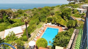 A rooftop pool with lounge chairs, surrounded by greenery and overlooking a coastal view. - Hotel Monti (Casamicciola Terme)