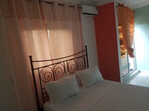 A bedroom with a bed, curtains, and an air conditioning unit. - Sea Side Apartments (Douala)