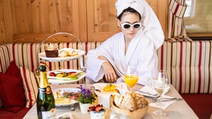 A person seated at a table with a variety of food items, a bottle of champagne, and glasses of wine. - Adults only Boutique - Hotel Unterlechner (Sankt Jakob in Haus)