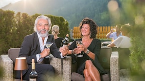 A couple seated on wicker outdoor furniture, holding wine glasses, with a bottle of wine on the table. - Adults only Boutique - Hotel Unterlechner (Sankt Jakob in Haus)