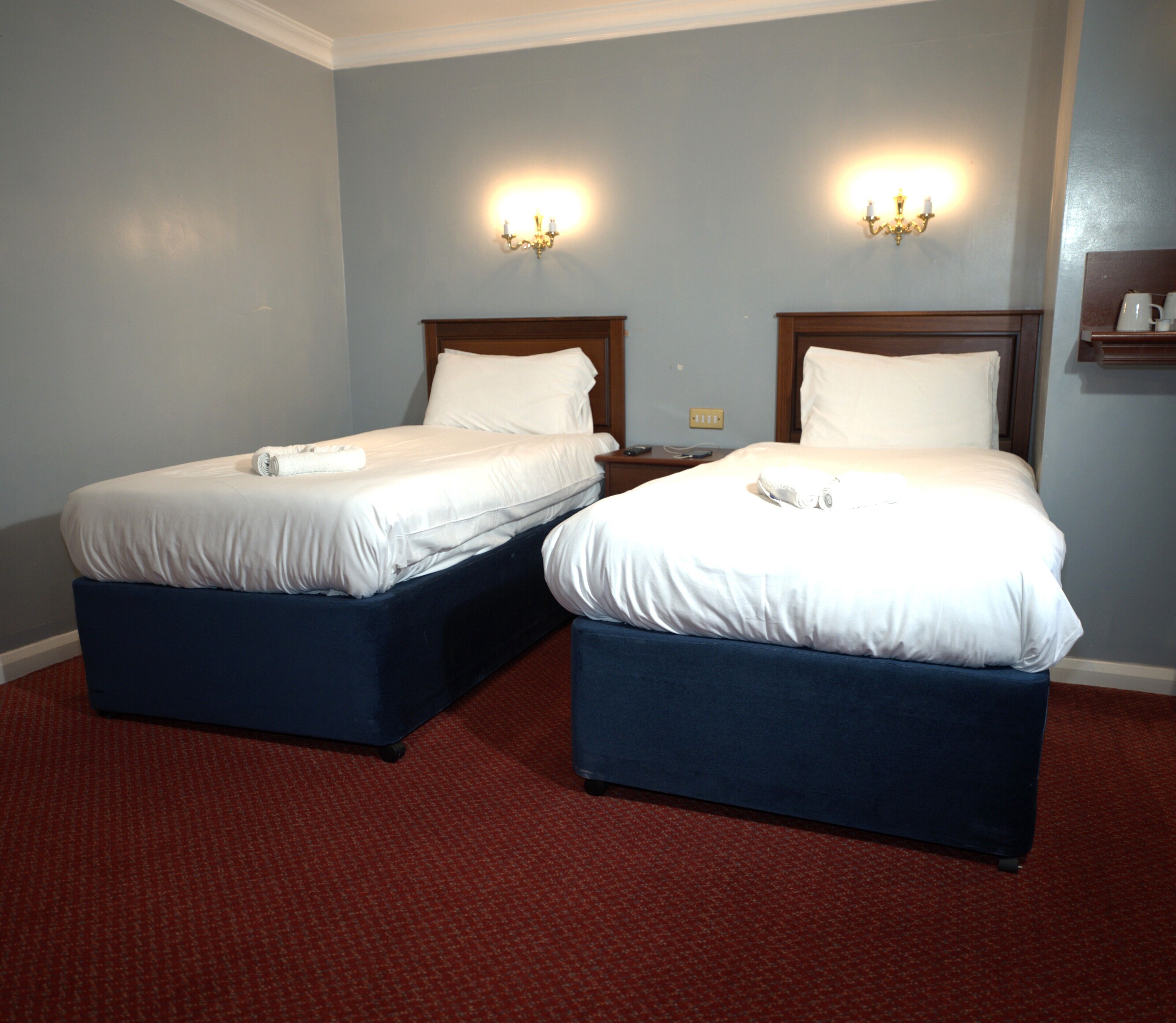 Camera d'albergo con due letti, ciascuno dotato di testata in legno, lenzuola bianche e tappeto rosso.