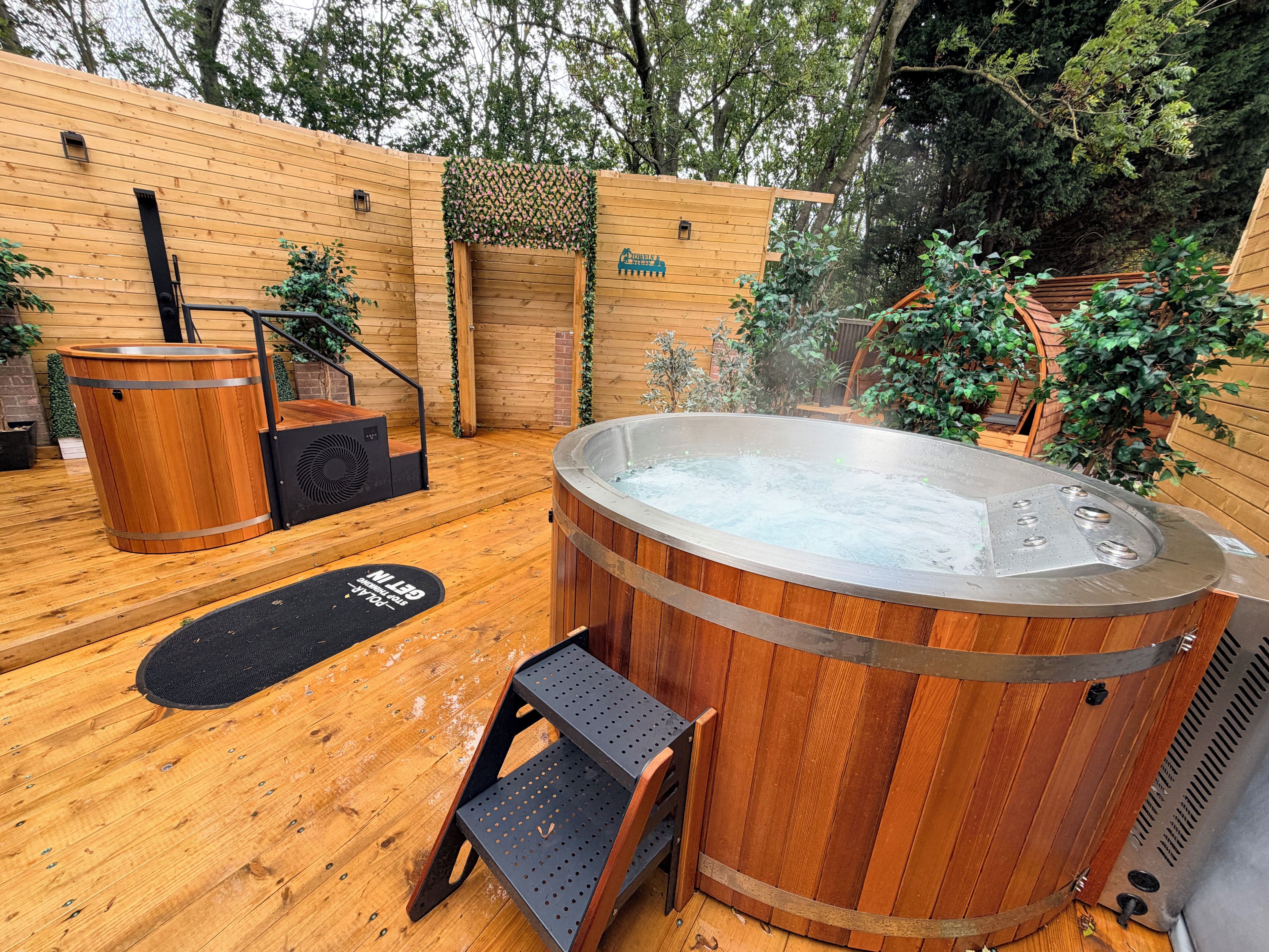 Una terraza de madera con un jacuzzi, un banco de madera y una pequeña mesa.