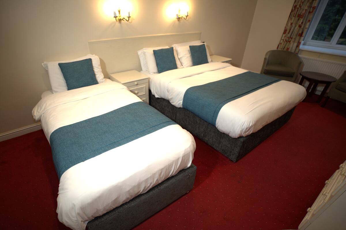 A hotel room with two beds, each with a white and blue bedspread, a red carpet, and a small table with a chair.