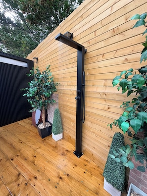 A wooden deck with a black metal structure, possibly a water feature, and potted plants.
