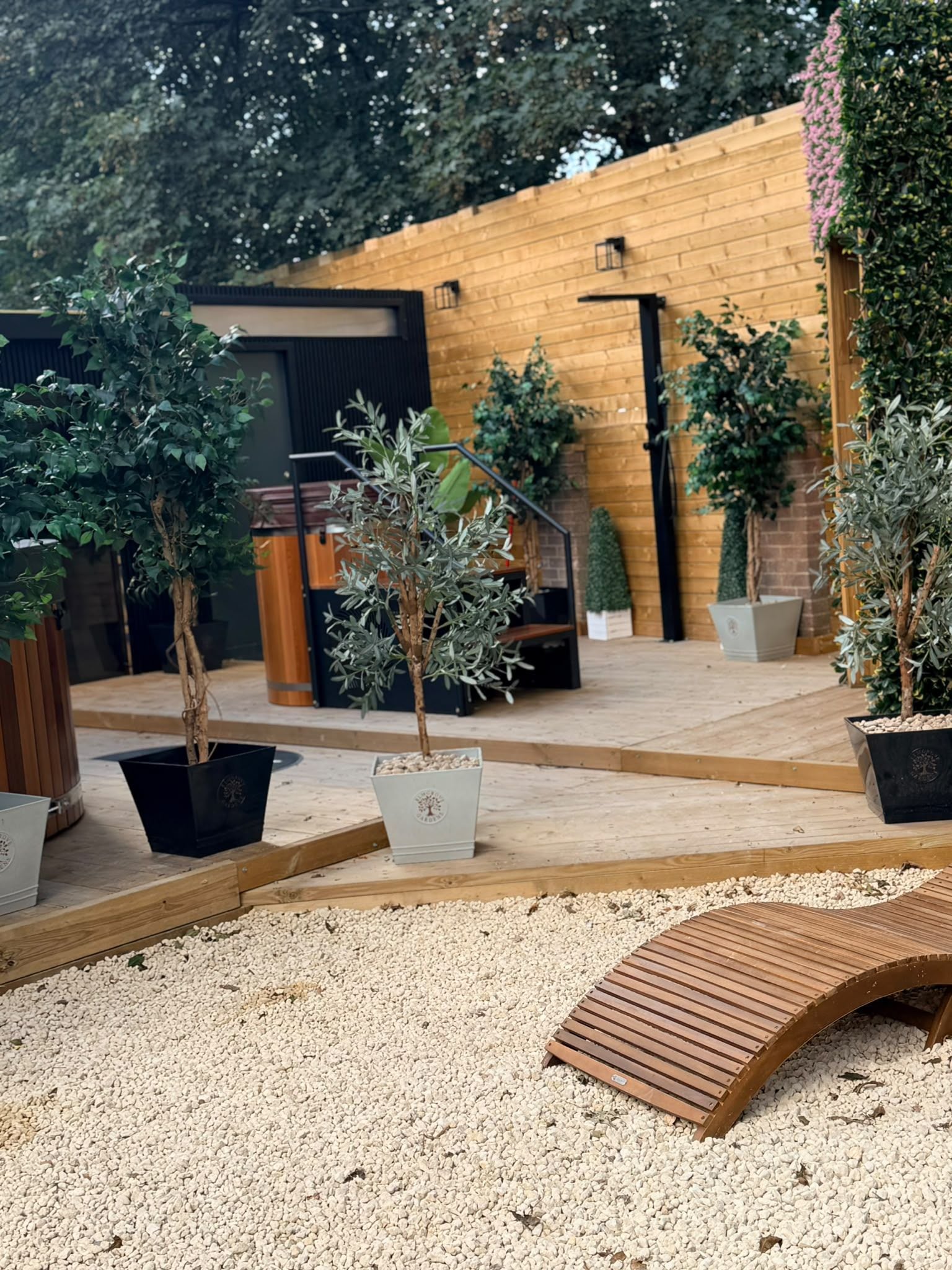 A garden area with potted plants, a wooden bench, and a building with a wooden facade.