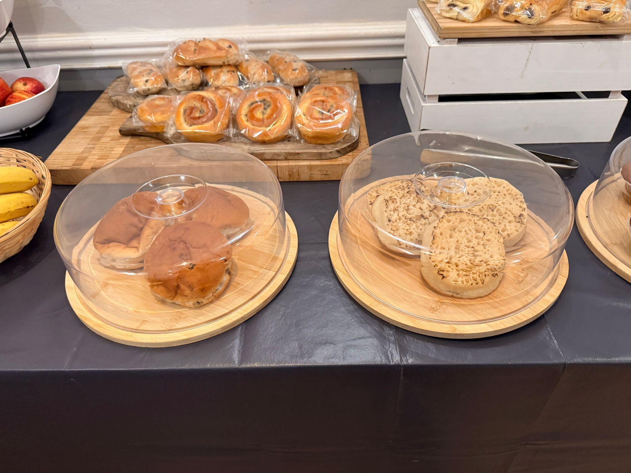 Una mesa de buffet con diversos productos de panadería, incluyendo pan y pastelería, exhibidos en recipientes transparentes.