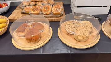 Una mesa de buffet con diversos productos de panadería, incluyendo pan y pastelería, exhibidos en recipientes transparentes.