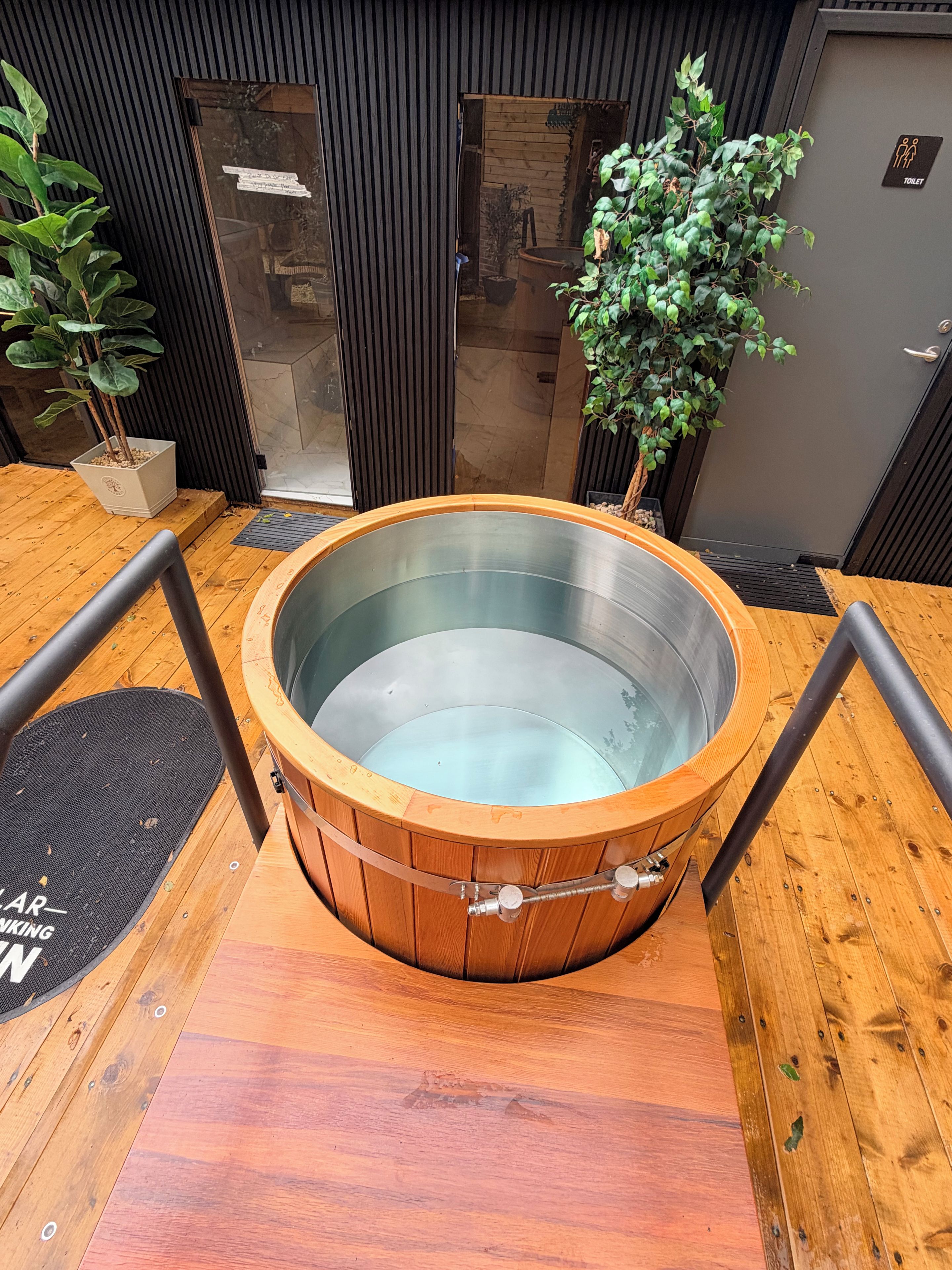 A wooden hot tub with metal sides, surrounded by wooden flooring and metal railings.