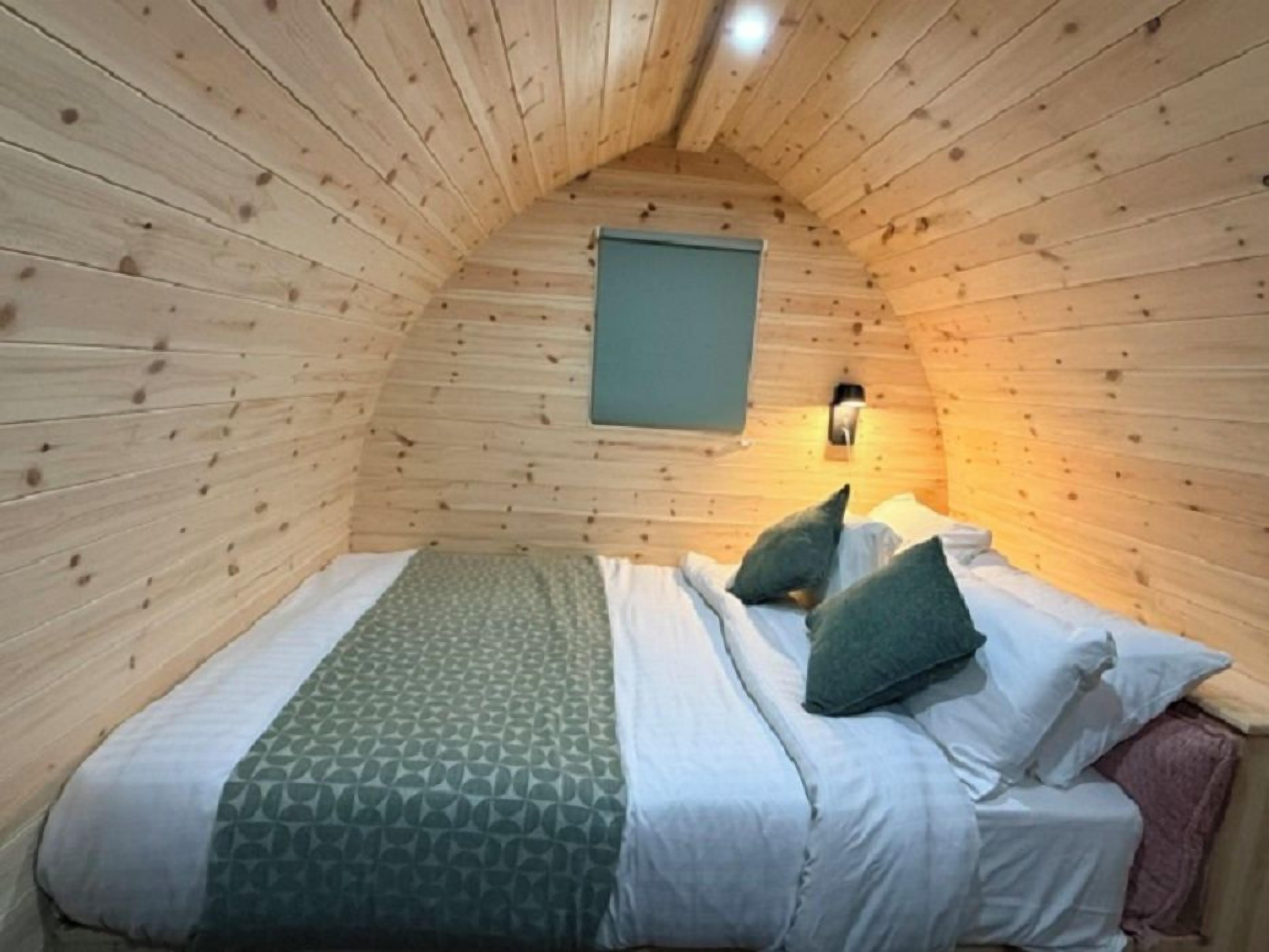 A cozy room with a sloped ceiling, a bed with pillows, a wall-mounted light, and a window.