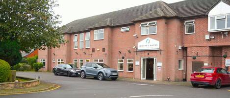 A brick building with a sign for 'CONSORT HOTEL' and two cars parked in front.