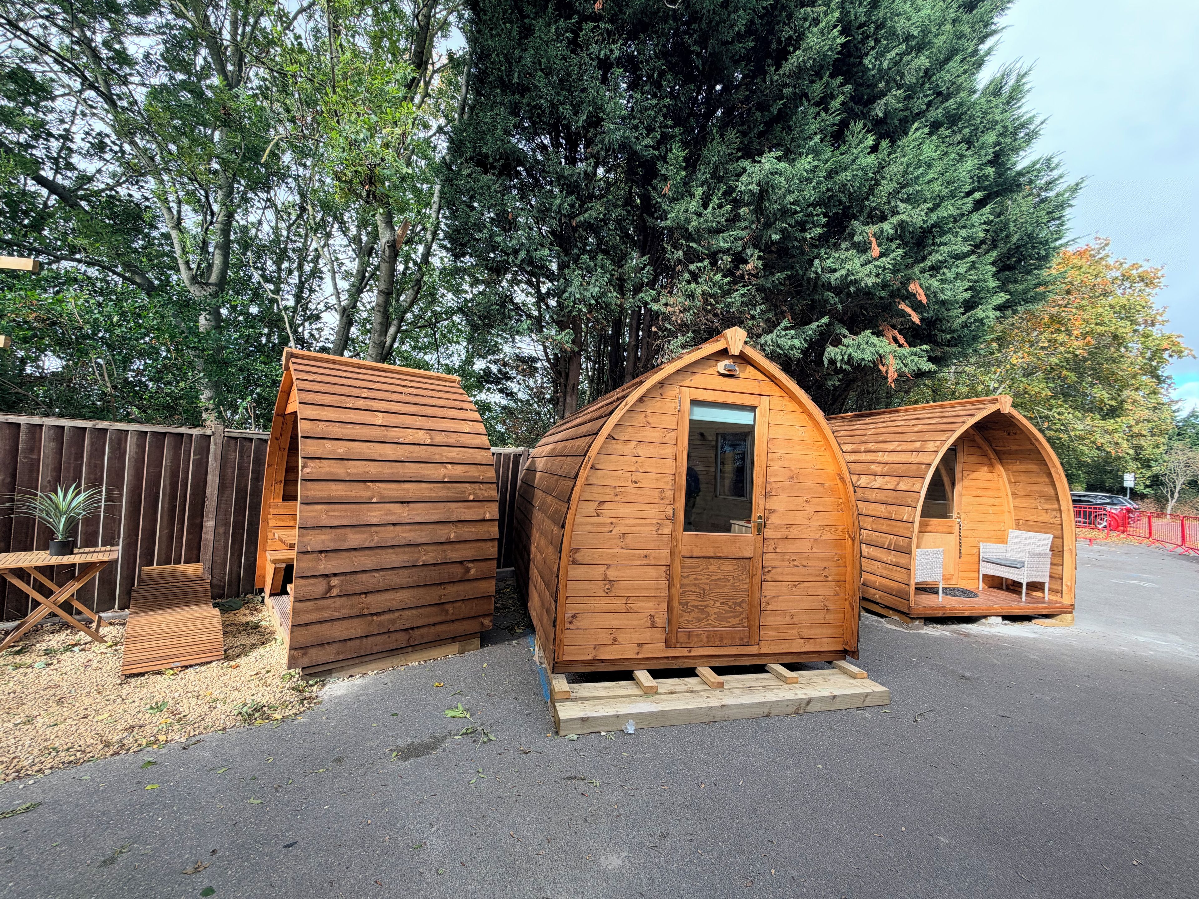 Tres cabañas de madera con techo a dos aguas, una puerta y un ventanal. Cada cabaña tiene un pequeño porche con un banco.