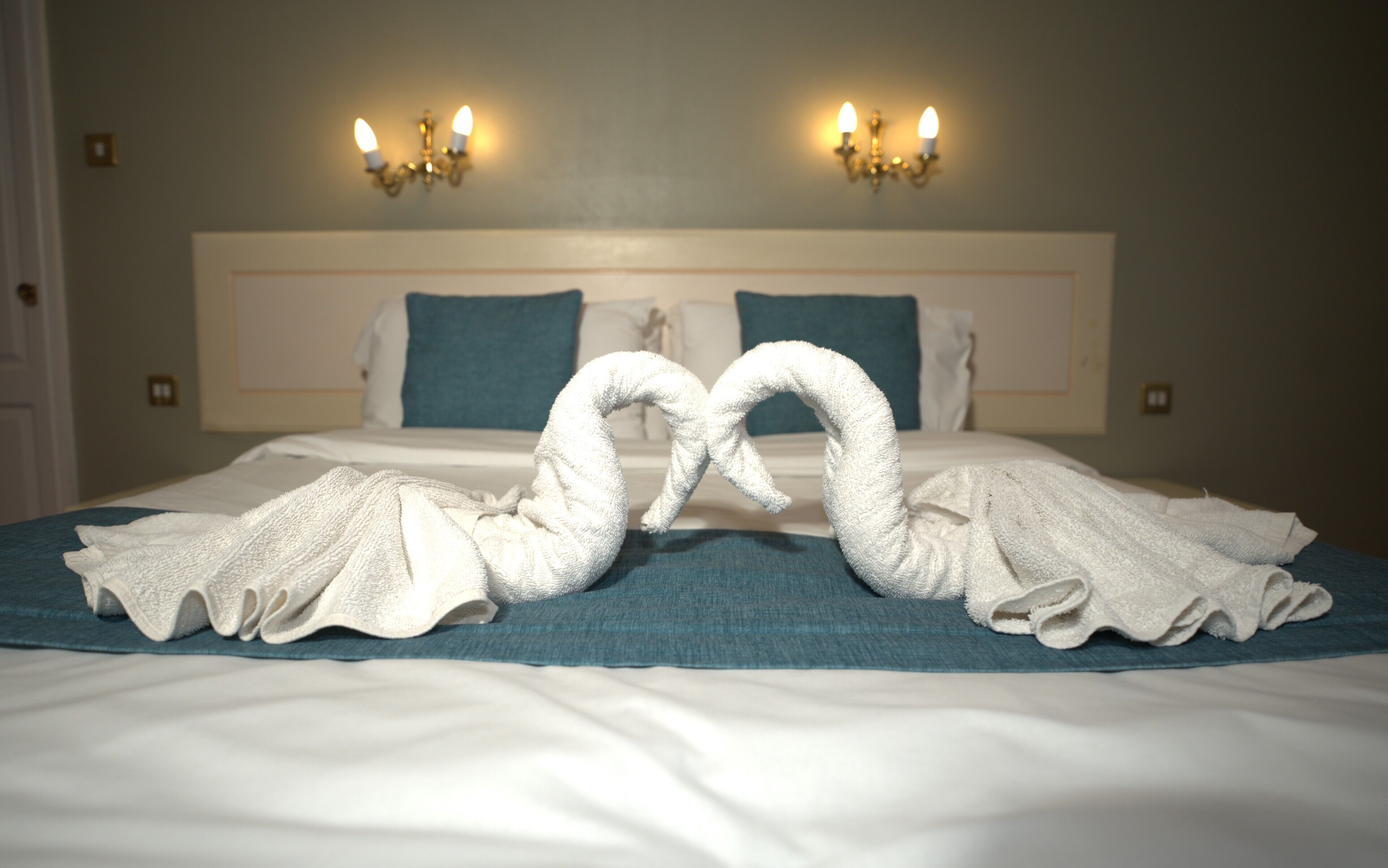 Une chambre d’hôtel avec un grand lit, deux lampes fixées au mur et une présentation décorative des serviettes.