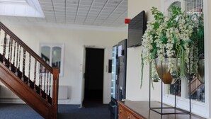 A hallway with a wooden staircase, a wall-mounted television, and a hanging floral arrangement. - Consort Hotel & Urban Spa (Rotherham)