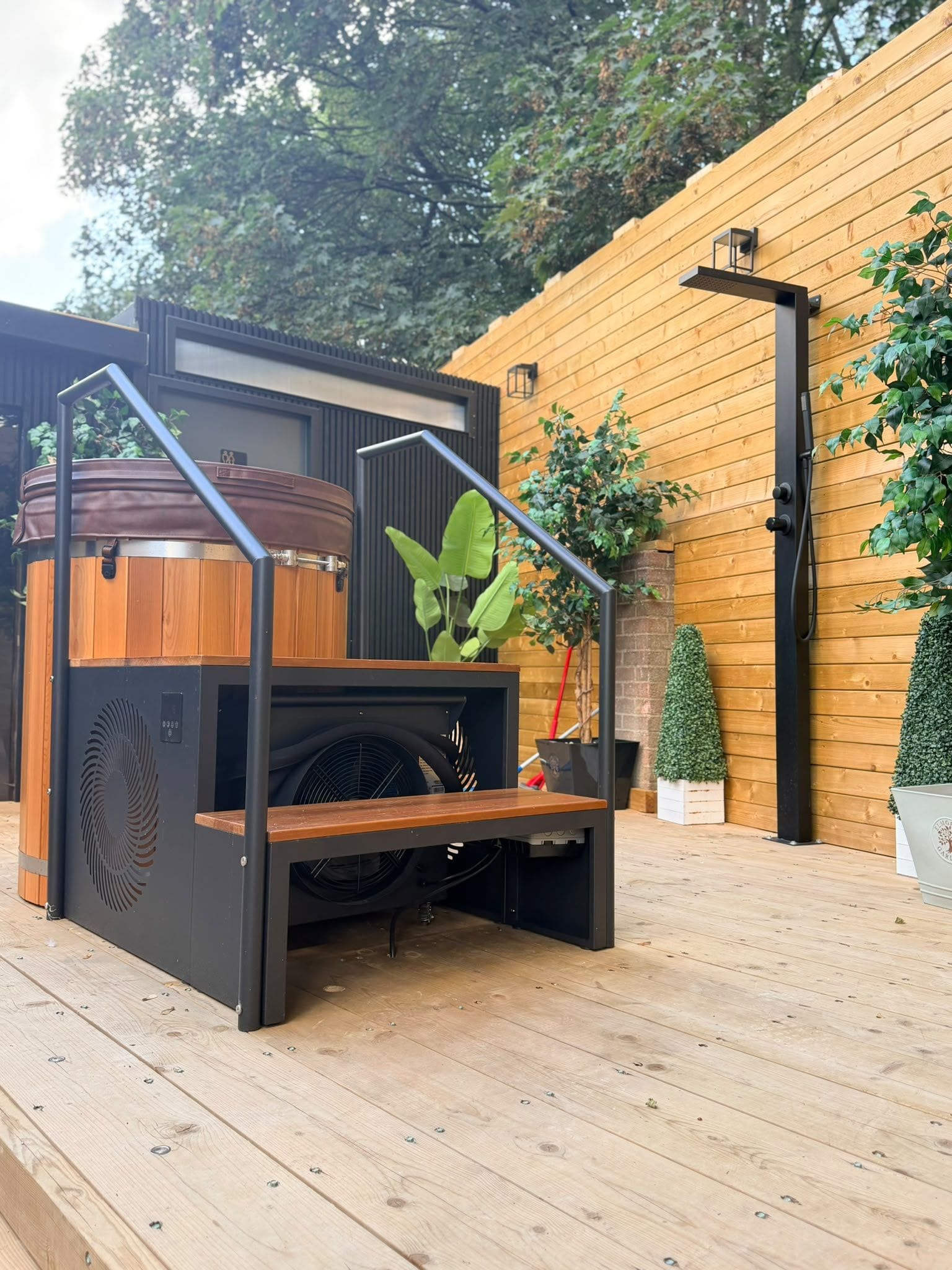 A modern outdoor kitchen with a built-in grill, wooden deck, and potted plants.