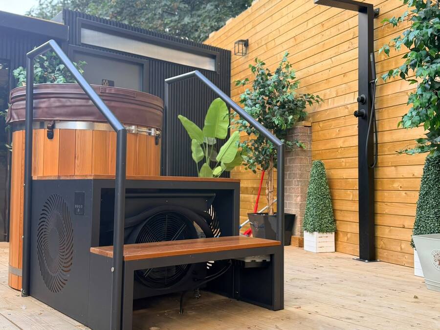 A modern outdoor kitchen with a built-in grill, wooden deck, and potted plants.