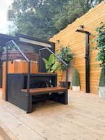 A modern outdoor kitchen with a built-in grill, wooden deck, and potted plants.