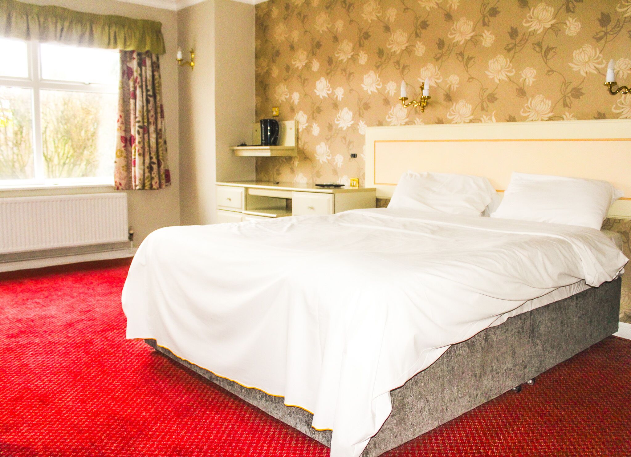 Une chambre d’hôtel avec un grand lit, une commode, une table de chevet et une fenêtre avec des rideaux.