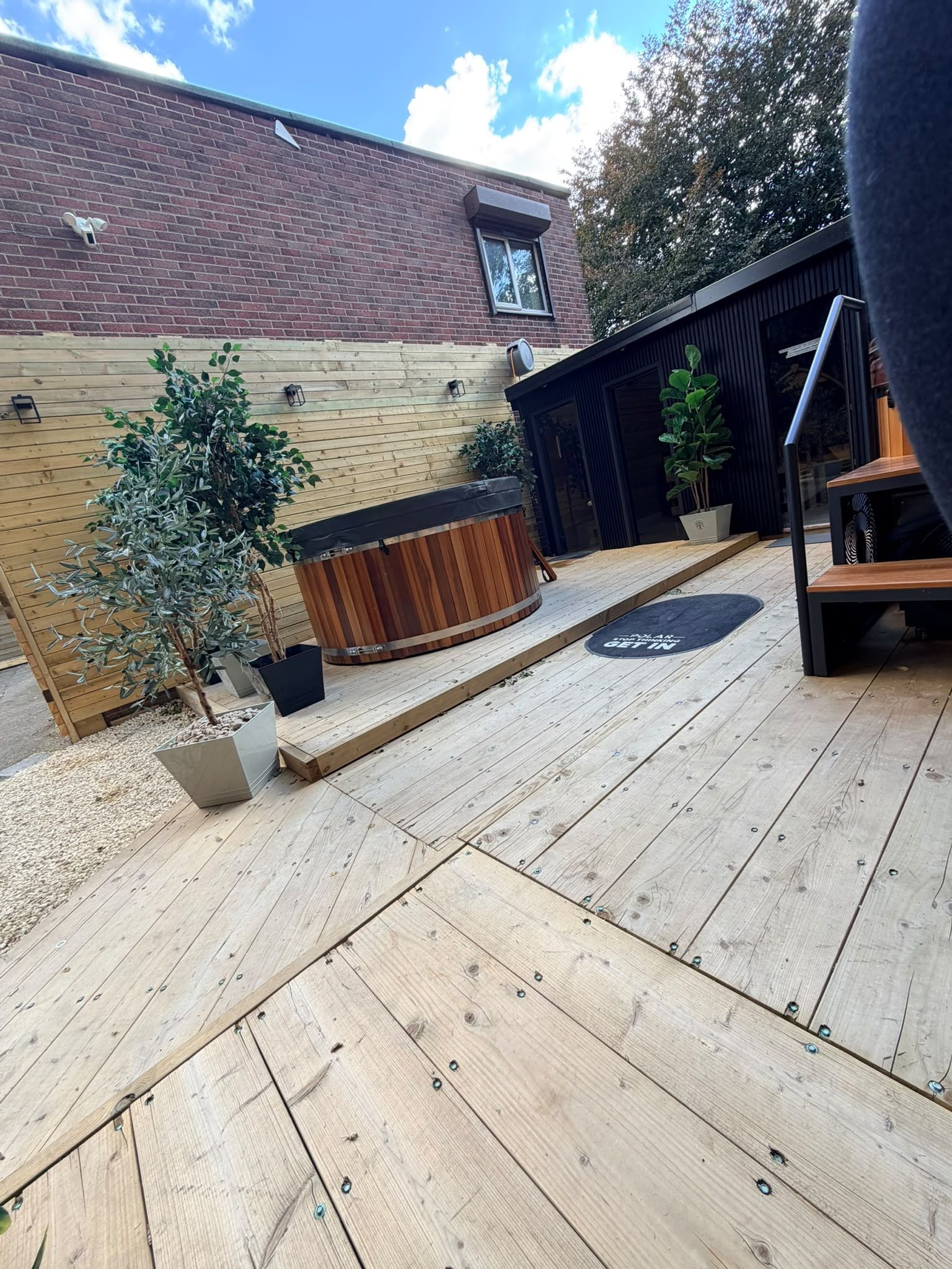 A wooden deck with a hot tub, potted plants, and a wooden fence.