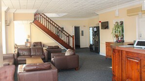 A spacious living area with leather sofas, a wooden staircase, a refrigerator, and a television on the wall. - Consort Hotel & Urban Spa (Rotherham)