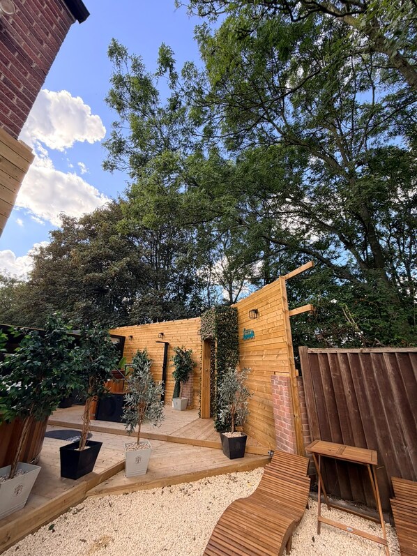 A wooden structure with a door, surrounded by trees and gravel. - Consort Hotel, Urban Spa & Glamping Pods (Rotherham)