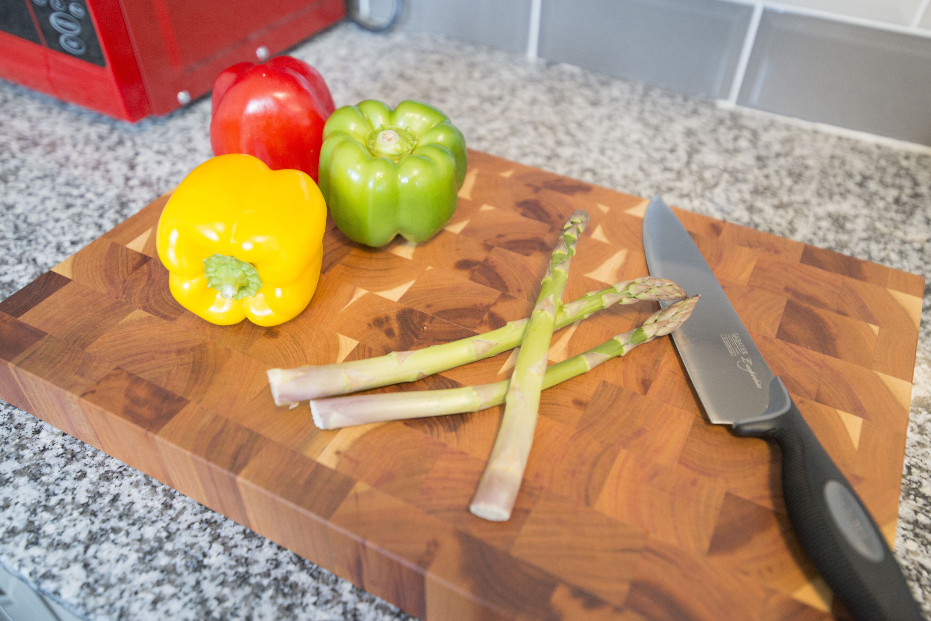 A wooden cutting board with vegetables and a knife on a kitchen counter.