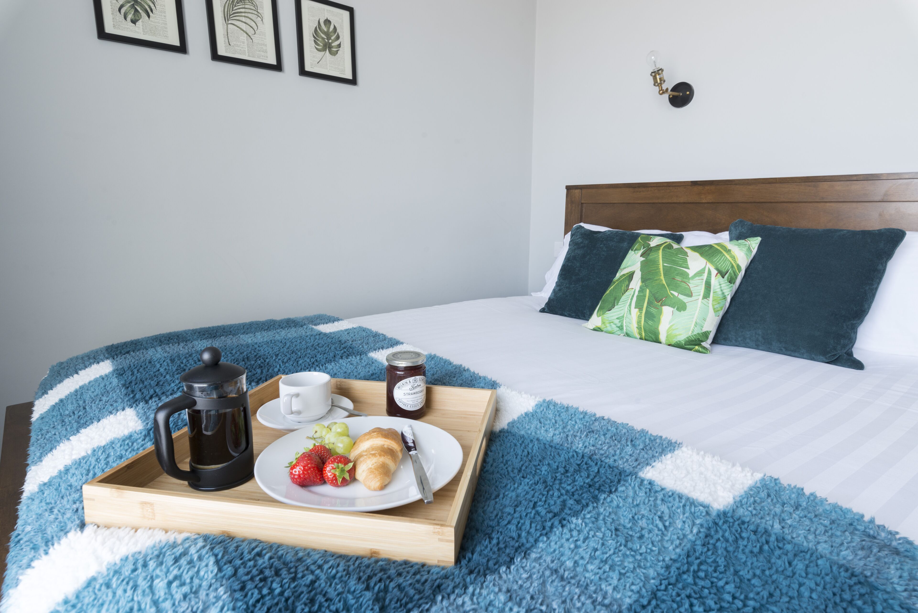A neatly made bed with a blue and white striped blanket, a wooden tray with breakfast items, and a wall with framed artwork.