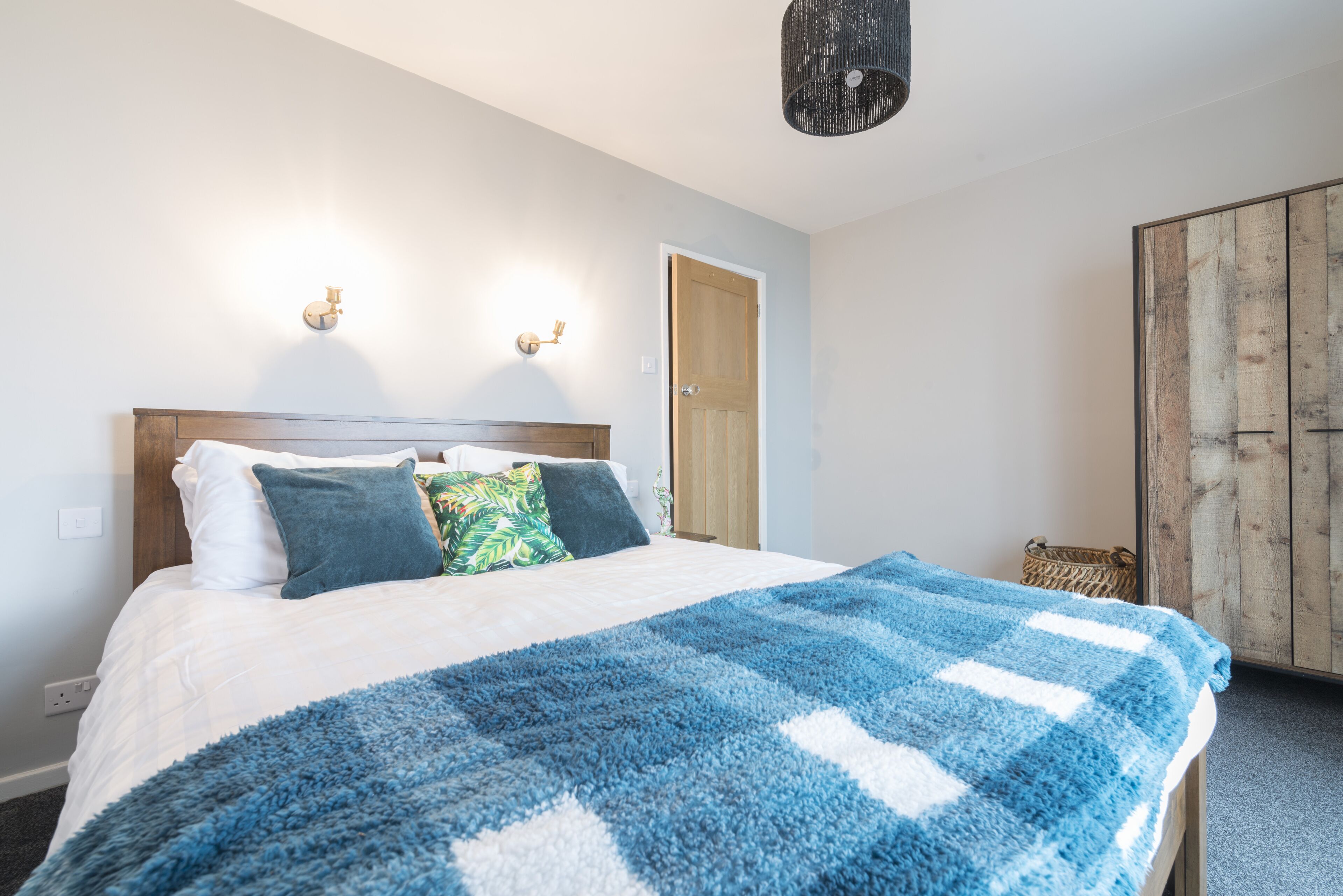 A bedroom with a bed, a blue and white blanket, and two wall-mounted lights.