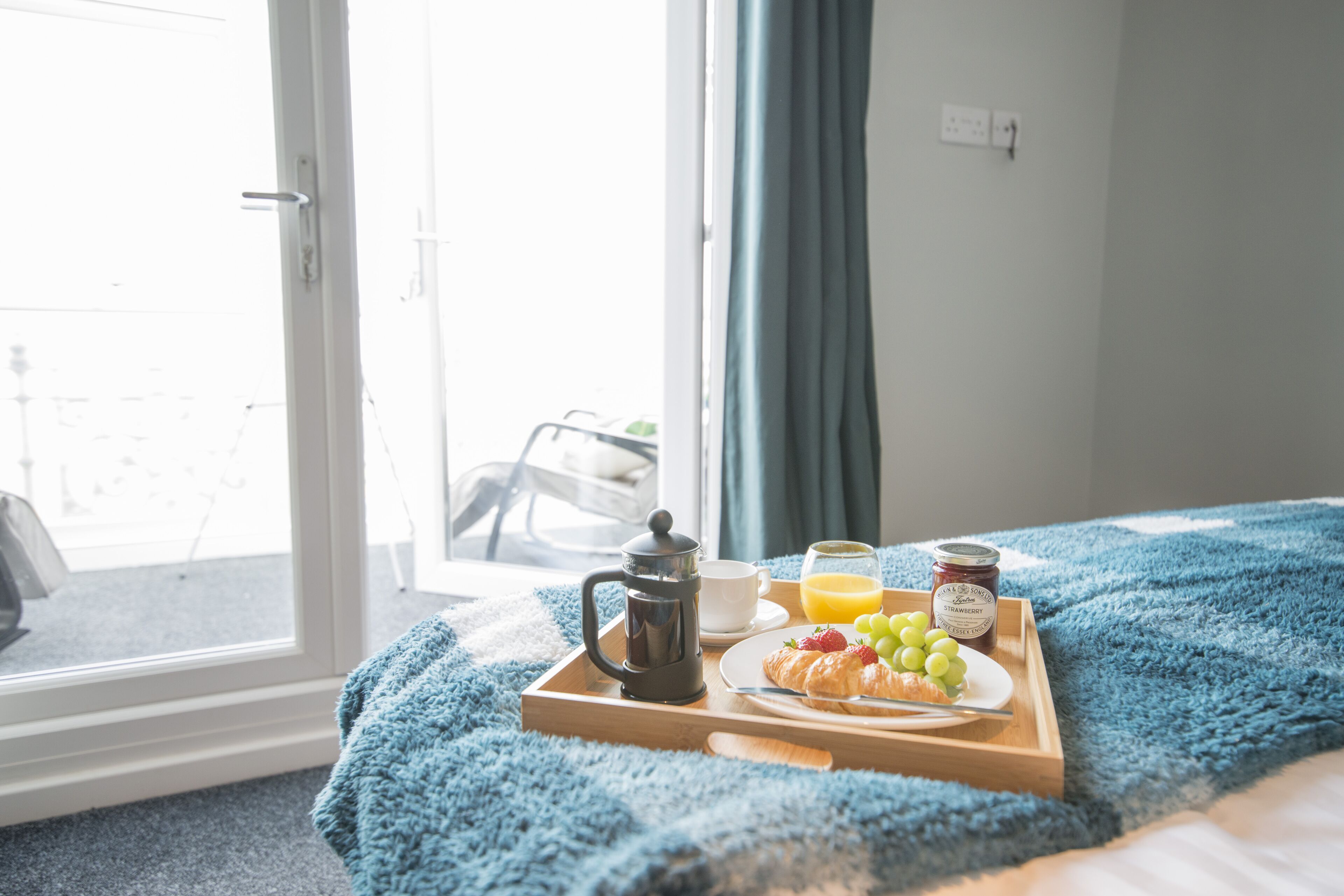 Bandeja de desayuno sobre la cama, con vista a un balcón.