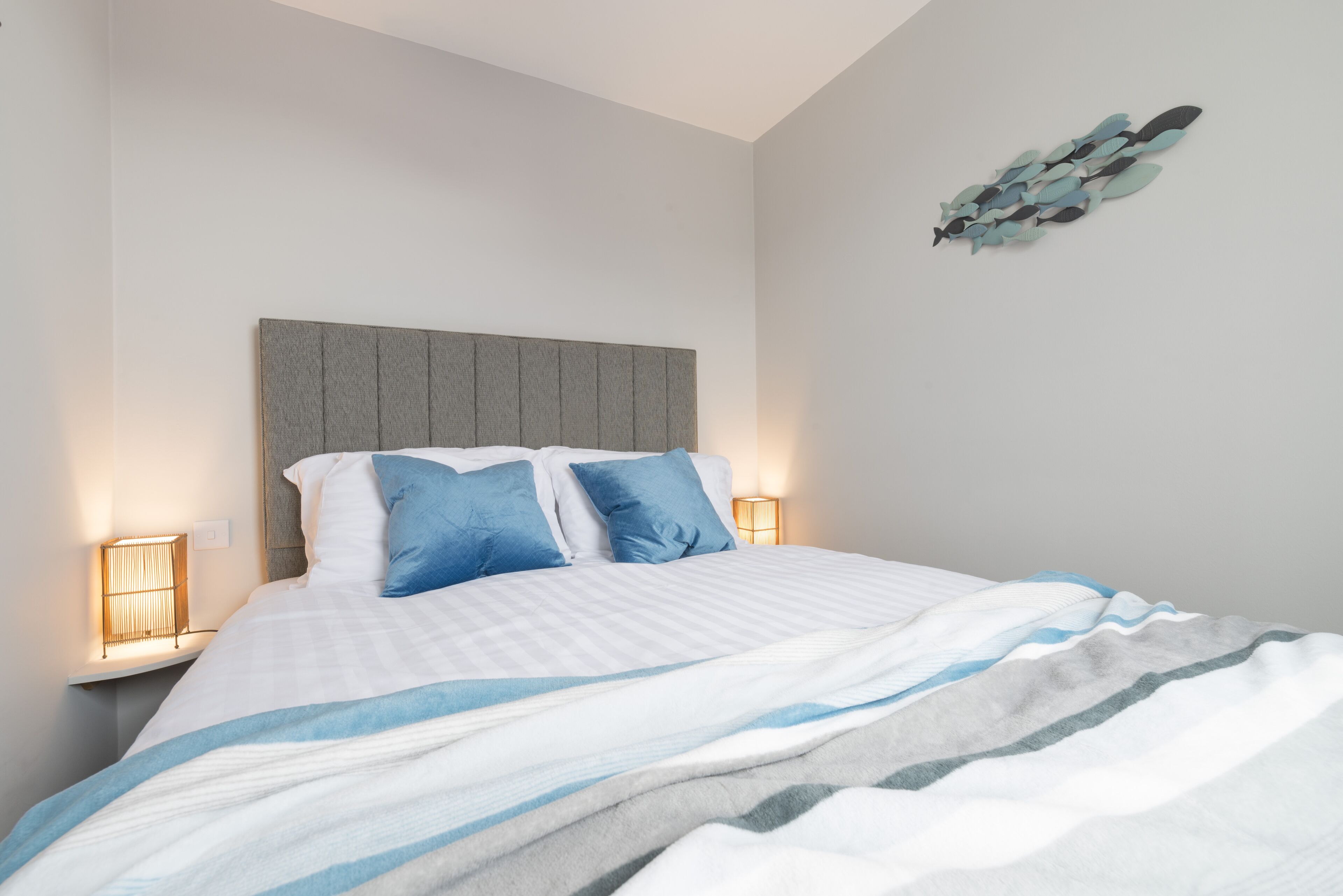 A neatly made bed with a striped bedspread, two blue pillows, and a gray headboard.