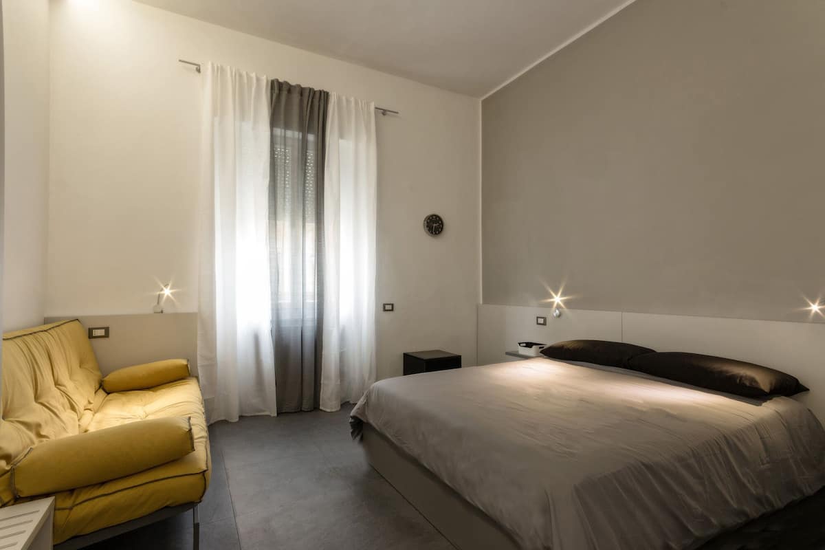 Una habitación de hotel moderna con una cama, una silla, una mesita de noche y un reloj de pared.