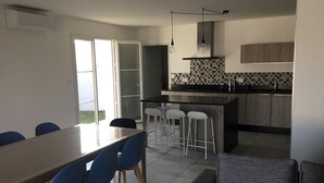 A modern kitchen with a central island, bar stools, and a dining table with chairs. - House the air of the wind (Saint-Denis-d'Oléron)