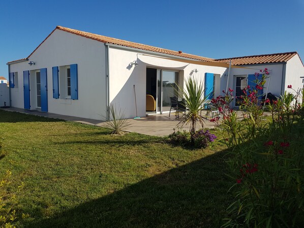 Una casa moderna con fachada blanca, contraventanas azules y techo de tejas.