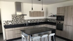 A modern kitchen with a central island, bar stools, a microwave, and a built-in oven. - House the air of the wind (Saint-Denis-d'Oléron)