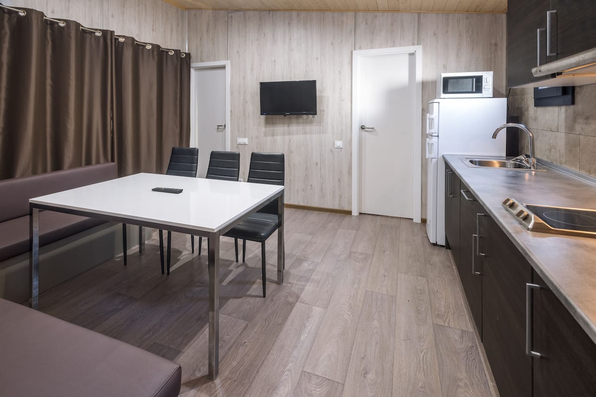 A compact kitchen with a dining area, a microwave, a sink, and a flat-screen TV mounted on the wall.