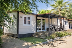 Une maison mobile de plain-pied, dotée d’une véranda, d’un petit jardin devant et d’un palmier.