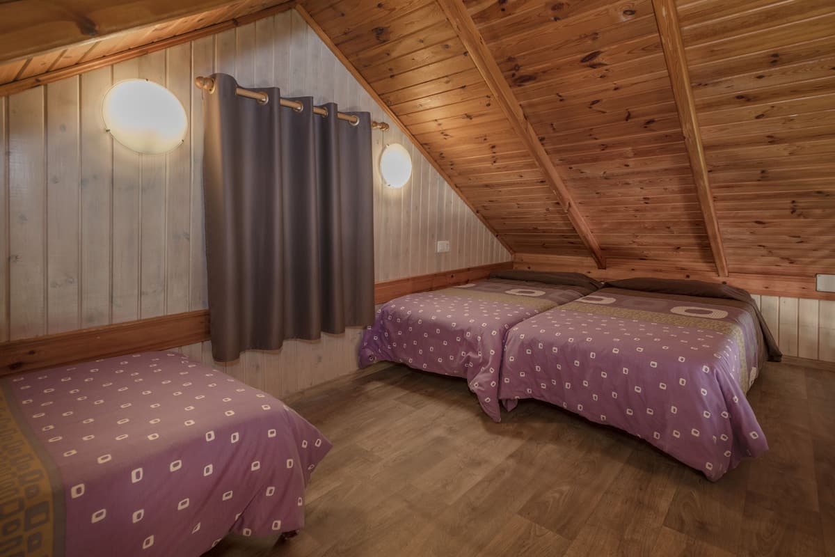 A room with two beds, wooden walls, and a sloped ceiling.